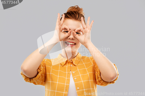 Image of red haired teenage girl making finger glasses