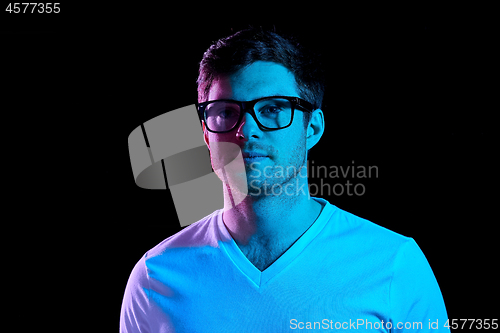 Image of man in glasses over neon lights in dark room