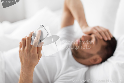 Image of hand of young man with smartphone in bed