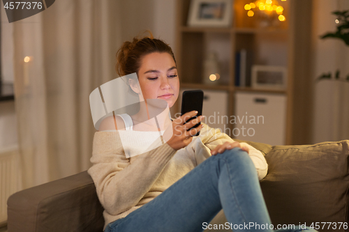 Image of young woman with smartphone at home in evening