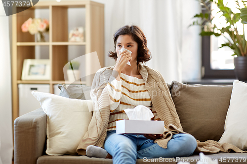 Image of sick woman blowing nose in paper tissue at home