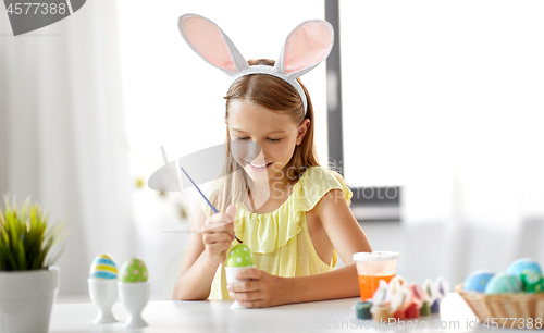 Image of happy girl coloring easter eggs at home