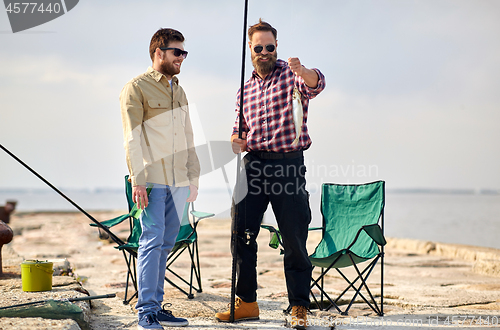 Image of happy friends with fish and fishing rods on pier