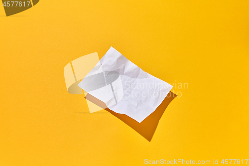 Image of Crumpled paper sheet with hard shadows on an yellow background.