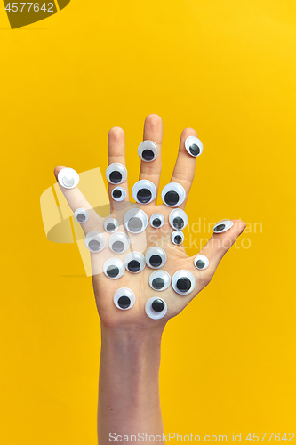 Image of Girl\'s hand with plastic eyes on an yellow background.