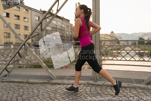 Image of woman jogging across the bridge at sunny morning