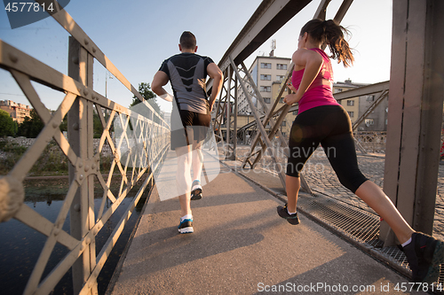 Image of young couple jogging across the bridge in the city