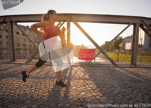 Image of woman jogging across the bridge at sunny morning