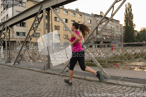 Image of woman jogging across the bridge at sunny morning