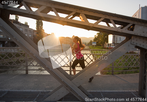 Image of woman jogging across the bridge at sunny morning