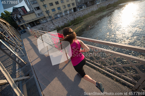 Image of woman jogging across the bridge at sunny morning