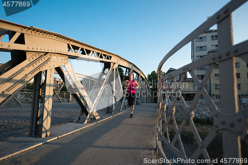 Image of woman jogging across the bridge at sunny morning