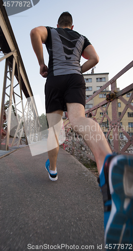 Image of man jogging across the bridge at sunny morning