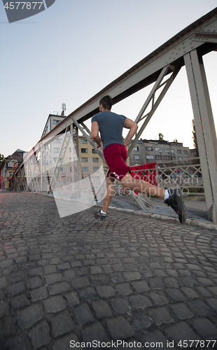 Image of man jogging across the bridge at sunny morning