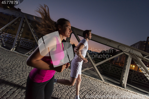 Image of couple jogging across the bridge in the city