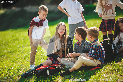 Image of A group of children of school and preschool age are sitting on the green grass in the park.