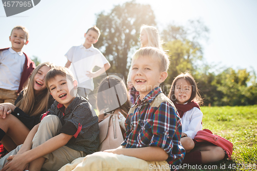 Image of A group of children of school and preschool age are sitting on the green grass in the park.