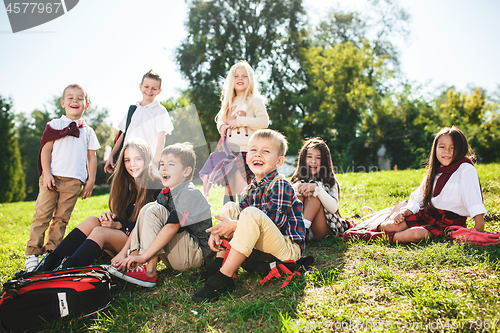 Image of A group of children of school and preschool age are sitting on the green grass in the park.