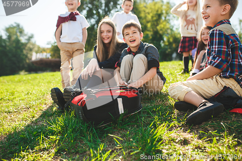 Image of A group of children of school and preschool age are sitting on the green grass in the park.