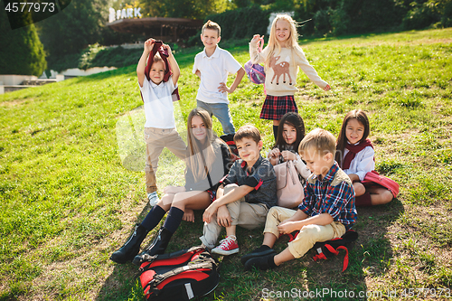 Image of A group of children of school and preschool age are sitting on the green grass in the park.