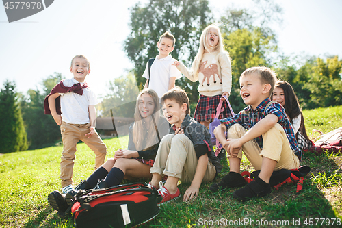 Image of A group of children of school and preschool age are sitting on the green grass in the park.