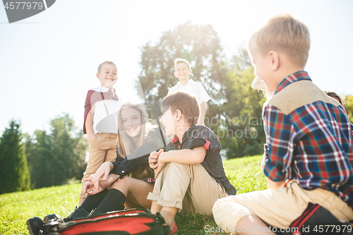 Image of A group of children of school and preschool age are sitting on the green grass in the park.