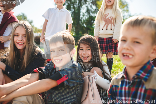 Image of A group of children of school and preschool age are sitting on the green grass in the park.