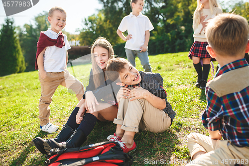 Image of A group of children of school and preschool age are sitting on the green grass in the park.