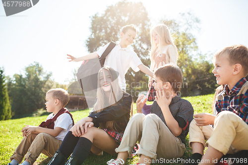 Image of A group of children of school and preschool age are sitting on the green grass in the park.