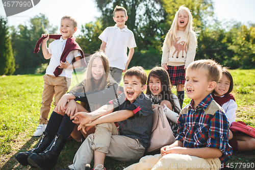 Image of A group of children of school and preschool age are sitting on the green grass in the park.