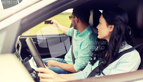 Image of happy couple in car taking selfie with smartphone