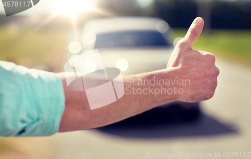 Image of man hitchhiking and stopping car with thumbs up