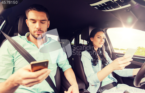 Image of man and woman with smartphones driving in car