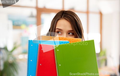 Image of teenage student girl hiding behind notebooks