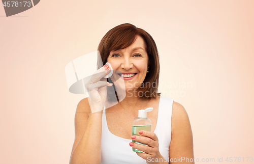 Image of senior woman cleaning face by lotion on cotton pad