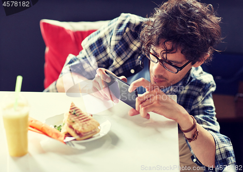 Image of man with smartphone photographing food at cafe