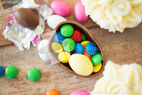 Image of chocolate egg with candies and cupcakes on table