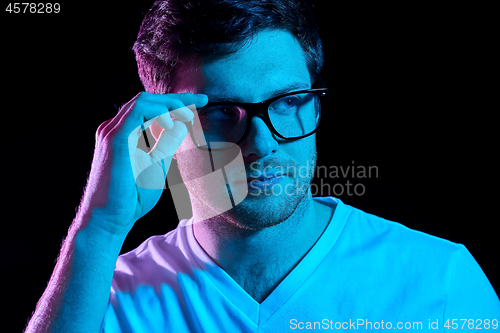 Image of man in glasses over neon lights in dark room