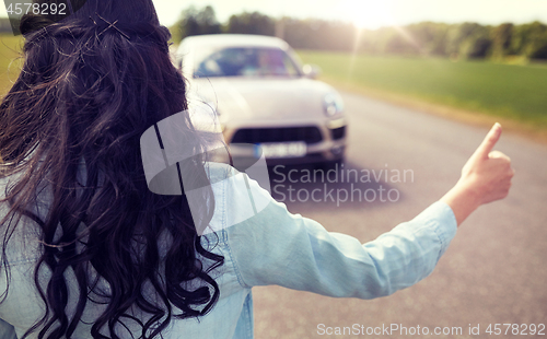 Image of woman hitchhiking and stopping car with thumbs up