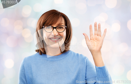 Image of portrait of senior woman in glasses waving hand