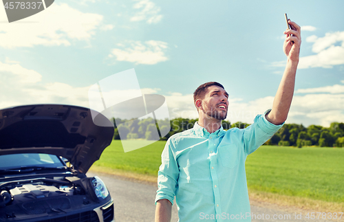 Image of man with smartphone and broken car at countryside