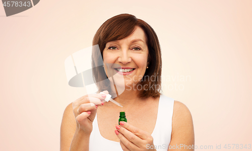 Image of smiling senior woman with bottle of serum