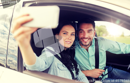 Image of happy couple in car taking selfie with smartphone