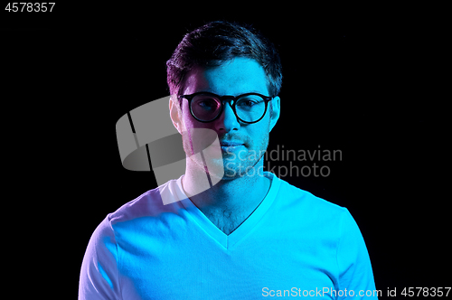 Image of man in glasses over neon lights in dark room