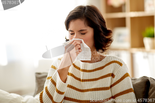 Image of sick woman blowing nose in paper tissue at home