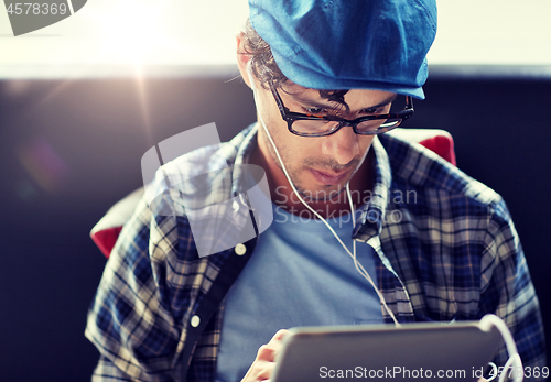 Image of man with tablet pc and earphones sitting at cafe