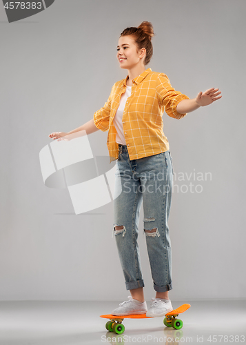 Image of red haired teenage girl riding on short skateboard