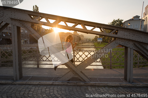 Image of woman jogging across the bridge at sunny morning