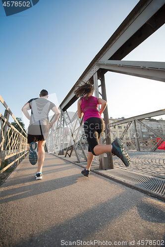 Image of young couple jogging across the bridge in the city