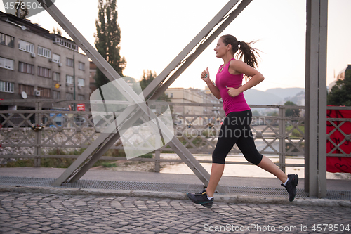 Image of woman jogging across the bridge at sunny morning